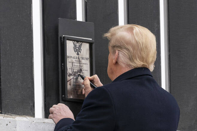 도널드 트럼프 미국 대통령이 12일(현지시간) 텍사스주 알라모의 미국-멕시코 국경장벽을 시찰하며 장벽에 부착된 명판에 서명하고 있다.(사진=AP.연합뉴스 제공)