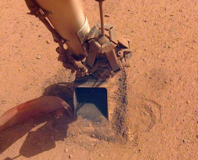 화성 두더지 장비(HP3)가 로봇팔의 주걱 도움을 받아 땅속으로 밀고 들어가는 모습. 나사 제공