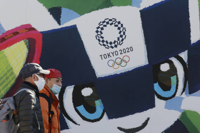 두 남성이 19일 일본 도쿄의 도쿄 올림픽 마스코트 미라이토와가 그려진 한 대형 포스터 앞을 지나고 있다.  도쿄 | AP연합뉴스