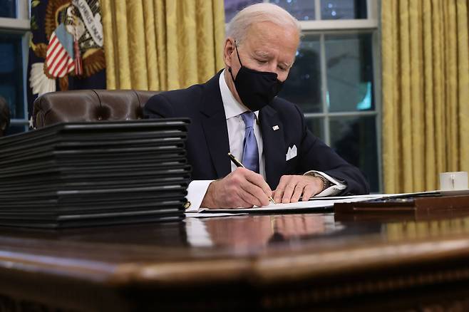 조 바이든 미국 대통령이 20일(현지 시각) 백악관 집무실 '결단의 책상(Resolute Desk)'에서 행정명령에 서명하고 있다. /AFP 연합뉴스