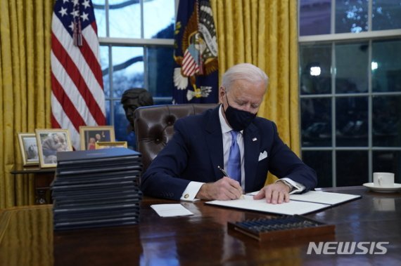 조 바이든 미국 대통령이 20일(현지시간) 백악관 집무실에서 첫 행정명령에 서명하고 있다. 바이든 대통령은 파리 기후변화 협약 복귀, 연방 시설 내 마스크 착용 의무화, 세계보건기구(WHO) 재가입 등에 관한 행정명령에 서명했다. / 뉴시스