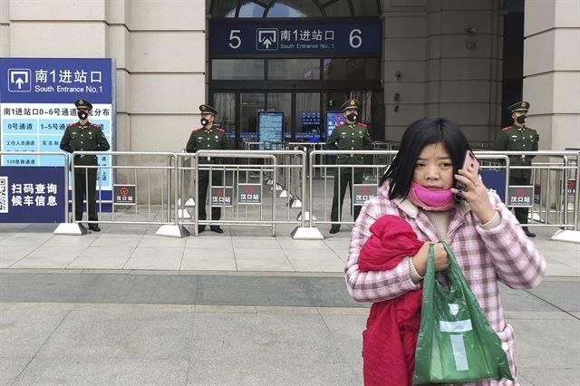 지난해 1월 23일 코로나19 확산으로 봉쇄령이 떨어진 중국 우한에서 한 여성이 폐쇄된 기차역 앞을 지나가는 가운데 뒤편에선 경찰들이 기차역 통행을 가로막고 있다. 우한=AP 뉴시스