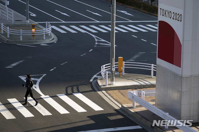 [도쿄=AP/뉴시스]21일 일본 도쿄에서 코로나19 예방을 위해 마스크를 쓴 한 여성이 2020 도쿄올림픽 광고판 근처 건널목을 건너고 있다. 2021.01.21.