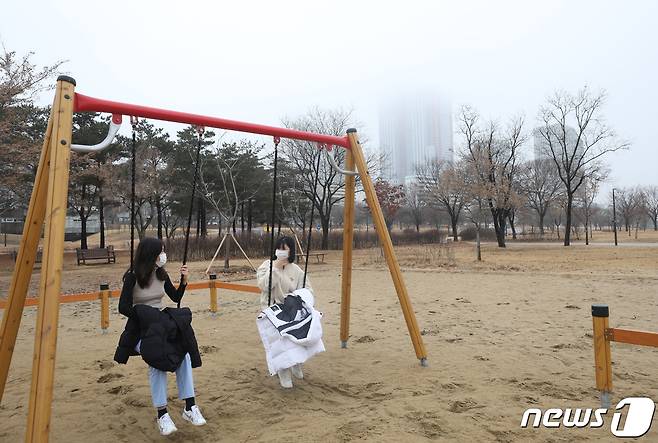 서울 여의도한강공원에서 그네를 타는 시민들 뒤로 보이는 고층 빌딩이 안개에 휩싸여 있다.© News1 신웅수 기자