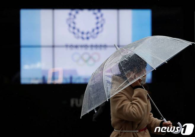 일본 도쿄의 한 행인이 도쿄올림픽 로고가 나오는 전광판 앞을 지나가고 있다. © 로이터=뉴스1