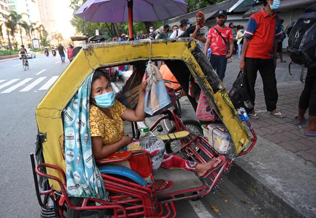 필리핀 수도 마닐라에서 한 여성이 집 역할을 하는 세발자전거 안에서 무료 배포하는 식량을 받기 위해 줄 서있는 남편을 기다리고 있다. 현재 필리핀은 코로나19 여파로 경제가 마비되고 실업자가 속출해 많은 이들이 빈민층으로 전락하고 있다. 마닐라=AFP 연합뉴스