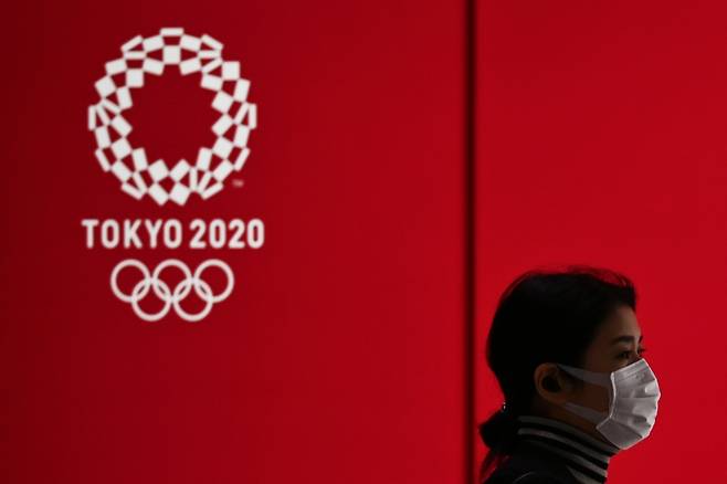 A woman in a face mask walks past a display showing the Tokyo 2020 Olympic Games logo in Tokyo on March 24, 2020. (AFP-Yonhap)