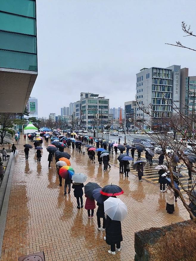 코로나19 진단검사 행정명령이 내려진 첫날인 26일 오후 경북 포항시청 앞에 마련된 선별검사소에서 비가 내리는 가운데 코로나19 검사를 받으려는 시민들이 길게 줄을 서 있다.