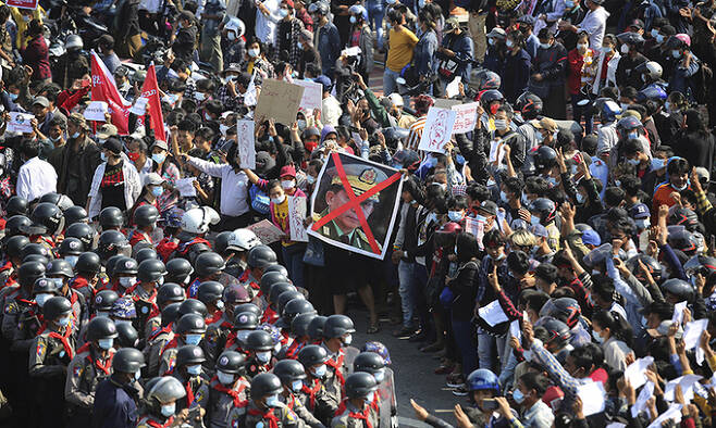 8일(현지시간) 미얀마 수도 네피도에서 쿠데타 항의 시위대가 'X' 표시가 된 민 아웅 흘라잉 군 최고사령관의 사진을 든 채 저항의 상징인 '세 손가락 경례'를 하며 경찰과 대치하고 있다. 네피도=AP연합뉴스