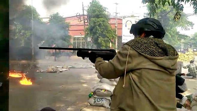27일(현지시간) 미얀마 제2 도시 만달레이에서 한 시위 참가자가 실탄 사격을 하는 군경을 향해 공기총을 발사하고 있다. [로이터]