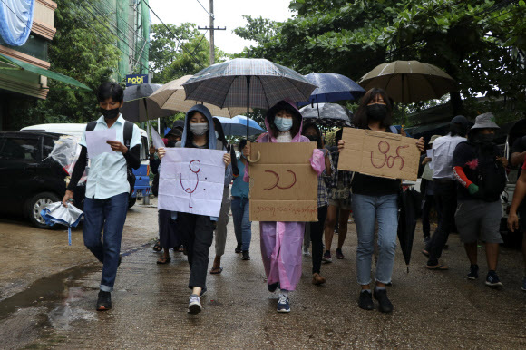 지난 6일(현지시간) 미얀마 양곤에서 우산을 쓴 반 쿠데타 시위대가 '빗물 시위'라고 쓰인 팻말을 들고 행진하고 있다. 양곤=AP·뉴시스