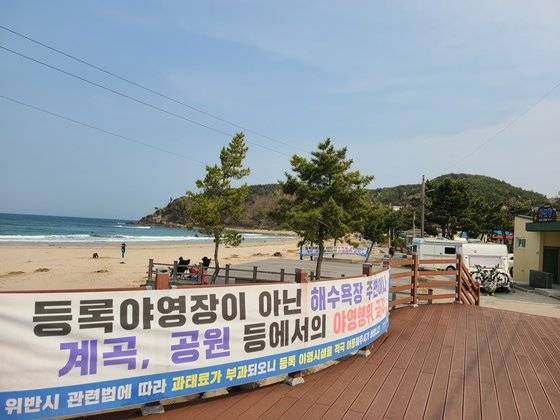 지난 11일 오후 강원 양양군 설악해변 데크에 ‘등록야영장이 아닌 해수욕장 주변이나 계곡, 공원 등에서의 야영행위 금지’라고 적힌 현수막이 걸려 있는 모습. 현수막 오른쪽엔 캠핑 트레일러가 주차돼 있다. 박진호 기자.