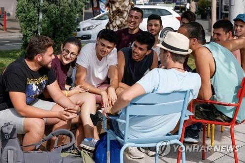 이스라엘이 실외 마스크 착용 의무를 해제한 첫날인 지난 18일(현지시간) 텔아비브 거리에서 젊은이들이 마스크를 벗은 채 붙어 앉아 이야기를 나누고 있다.[AFP=연합뉴스 자료사진]