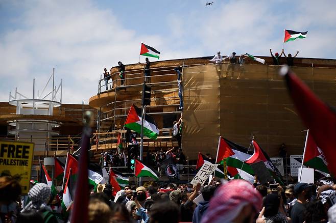 LA에서 집회에 참석한 사람들이 건물에 올라가 팔레스타인 깃발을 흔들고 있다. AFP=연합뉴스