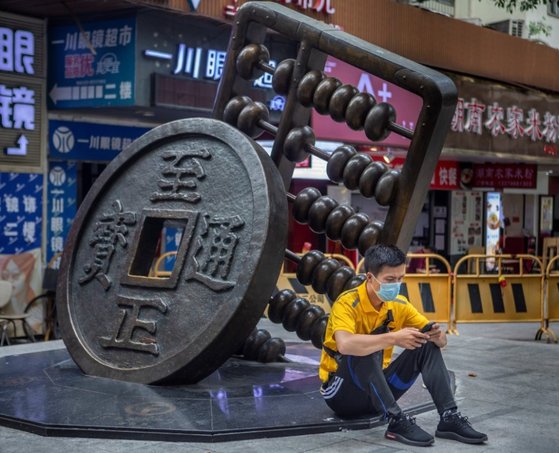 중국 광둥성 광저우의 한 거리에서 한 시민이 마스크를 쓴 채 화폐와 주판 조각상 옆에 앉아 스마트폰을 보고 있다. [연합뉴스]