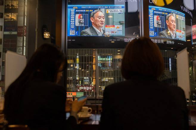 도쿄 한 카페에서 두 여성이 스가 요시히데 일본 총리가 지난 5월 긴급사태 연장을 발표하는 모습을 지켜보고 있다(사진=AFP)
