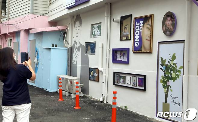 경북 김천예고 옆 교동연화지로 가는 골목길에 조성된 '트바로티 김호중 소리길' 담장 갤러리에 전시된 김호중 사진들을 지나가는 시민이 카메라에 담고 있다. 2021.9.20/뉴스1 © News1 정우용 기자