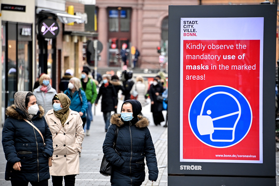 Pedestrians walk past a sign indicating that masks are mandatory in the marked areas in Bonn, Germany, March 13. In Germany, many stores that had been closed for months have opened again. [EPA/YONHAP]