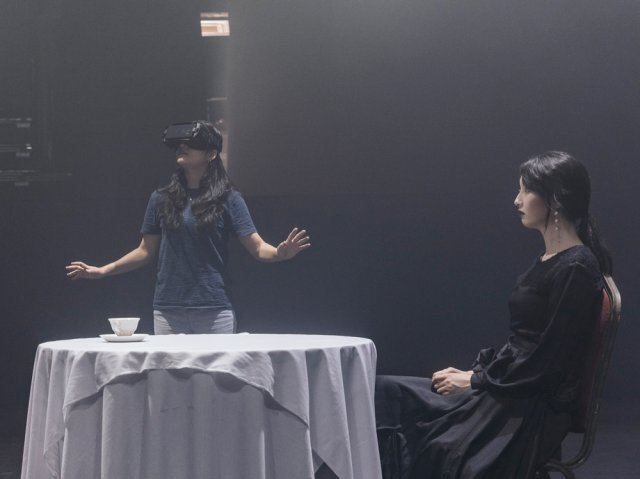 ‘코오피와 최면약’에서 가상현실(VR) 기기를 착용한 관객과 화면 속 배우(오른쪽)를 함께 촬영했다. 관객이 실제 보는 화면에는 테이블에 앉은 배우만 나타난다. 국립극단 제공