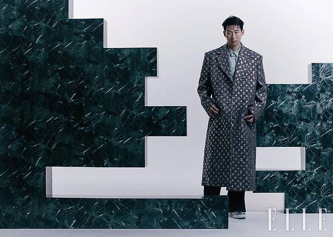 모노그램 패턴의 맥시 코트와 스트라이프 셔츠, 팬츠, 스니커즈는 모두 Louis Vuitton Men’s Collection.