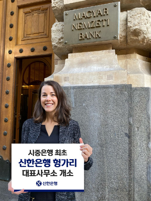A Shinhan Bank Hungary office employee poses for a photo in front of the Hungarian National Bank in Budapest with a sign marking the opening of the Korean bank’s office in the central European nation, in this photo released Thursday. (Shinhan Bank)