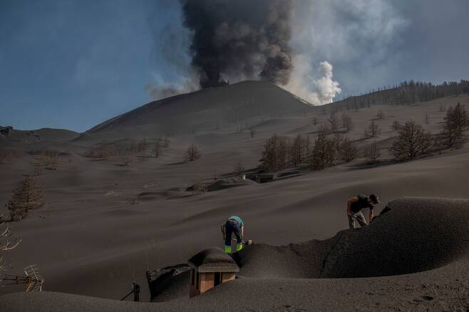 10월 14일 스페인 카나리아제도 라팔마섬 라스 만차스 지역에서 주민들이 지붕위에 쌓인 화산재를 치우고 있다./AP 연합뉴스