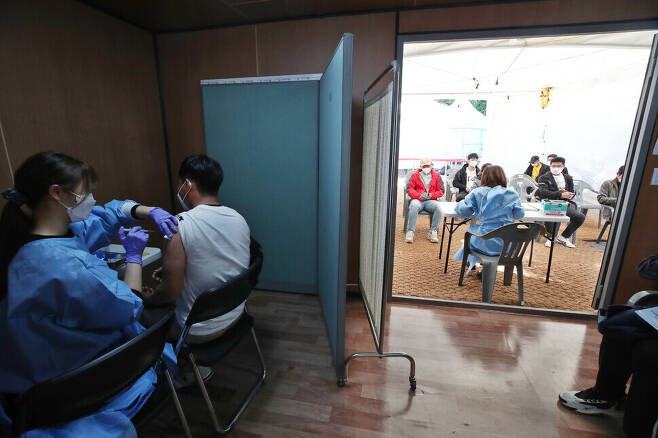 A person receives their COVID-19 vaccination at a vaccination site in Seoul’s Yeongdeungpo District on Sunday morning. On the righthand side of the photo, people who have received their vaccination can be seen sitting in a waiting room as they monitor for possible adverse reactions. (Baek So-ah/The Hankyoreh)