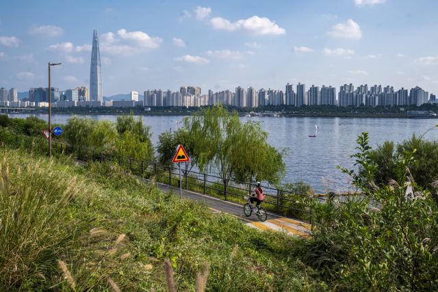 뚝섬한강공원에서 내려다본 한강과 서울 전경. 자전거를 타고 지나가는 시민 뒤로 한강에서 수상 레저를 즐기고 있는 모습이 보인다.