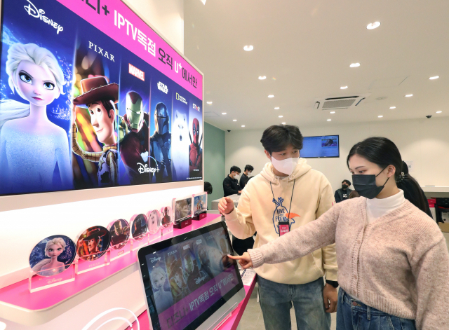 SK브로드밴드가 국내 IPTV로는 처음으로 애플과 손을 잡고 지난달 4일부터 한국 B tv 고객에게 애플TV 4K를 제공 중이다. 모델이 애플TV 4K를 소개하고 있다.(위쪽) LG유플러스 강남직영점 방문자가 디즈니플러스 체험존을 살펴보고 있다. [SK브로드밴드·LG유플러스 제공]