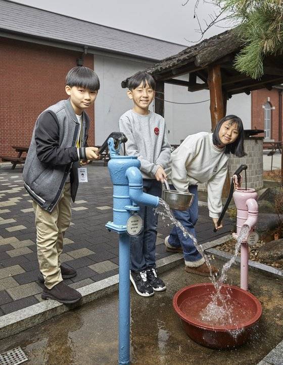 김휘윤 학생모델과 최주영 학생기자, 노윤채 학생모델(왼쪽부터)이 물 한 바가지를 펌프에 넣고 작두를 움직이면 물이 밑에서 쏟아져 나오는 작두 펌프를 직접 조작해봤다. 지금의 꼭지만 틀면 콸콸 나오는 수돗물과는 다른 형태다.