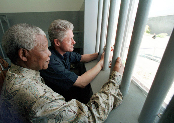 지난 2013년 세상을 떠난 넬슨 만델라 남아공 대통령이 18년 동안 수감돼 있던 루벤섬 교도소의 감방을 1998년 3월 27일(현지시간) 빌 클린턴 전 미국 대통령과 함께 찾아 안에서 밖을 내다보며 감회에 젖고 있다.AP 자료사진 연합뉴스