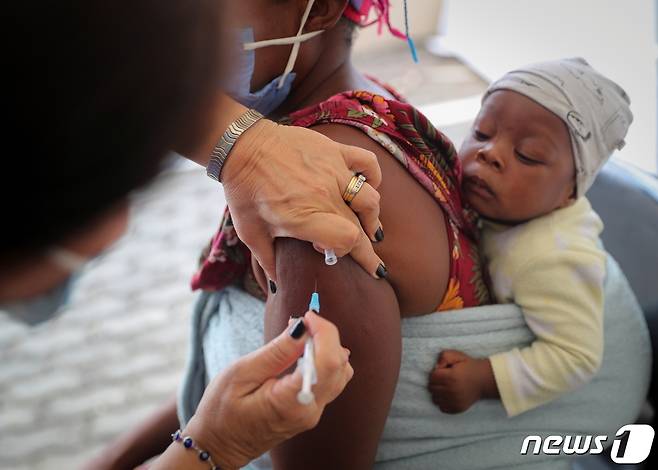 남아프리카공화국 요하네스버그 코로나19 접종소에서 2021년 12월 4일 한 여성이 아이를 업은 채 백신을 맞고 있다. © 로이터=뉴스1 © News1 최서윤 기자