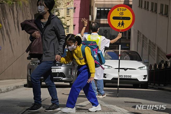[홍콩=AP/뉴시스] 11일 홍콩에서 한 초등학교 학생이 보호자와 함께 거리를 건너고 있다. 캐리 람 홍콩 행정장관은 어린이들의 코로나19 감염 사례가 늘면서 유치원과 초등학교를 일정 기간 폐쇄한다고 밝혔다. 2022.01.11