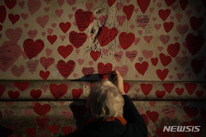 [런던=AP/뉴시스] 12일(현지시간) 영국 런던의 국립 코로나19 추모 벽에서 한 여성이 사랑의 하트 메모지에 고인에 대한 추모 메시지를 쓰고 있다. 2022.01.13.