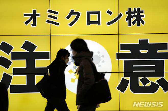 [도쿄=AP/뉴시스] 지난 24일 일본 도쿄에서 마스크를 쓴 시민들이 오미크론 변이에 대한 주의를 알리는 안내판 앞을 지나고 있다. 2022.01.25.
