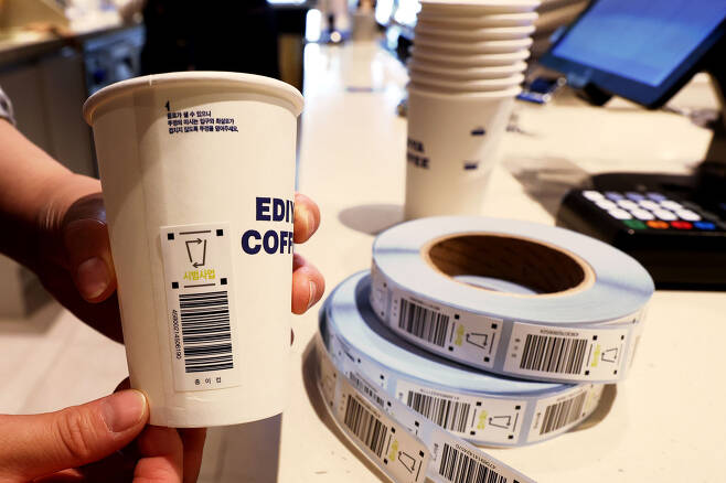 A worker attaches a “recyclable label" on a disposable cup at a coffee shop in central Seoul on May 6. (Joint Press Corps)