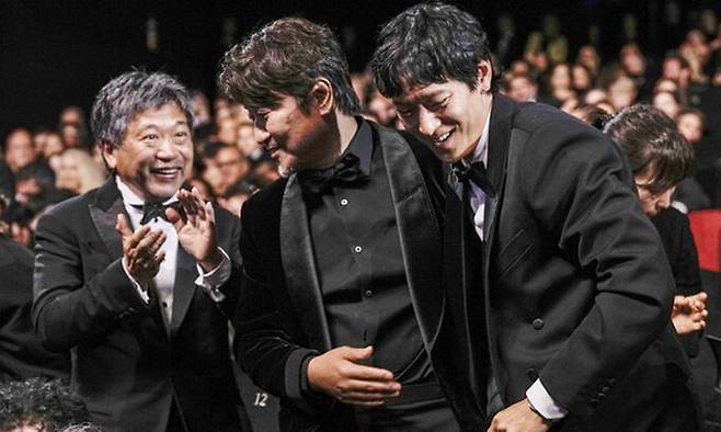 호명된 순간 배우 송강호(가운데)가 28일(현지시간) 프랑스 칸 뤼미에르 대극장에서 열린 제75회 칸국제영화제 시상식에서 남우주연상 수상자로 호명되자 옆자리에 앉은 고레에다 히로카즈 감독(왼쪽)과 배우 강동원의 축하를 받으며 무대로 나서고 있다. 칸=AP연합뉴스