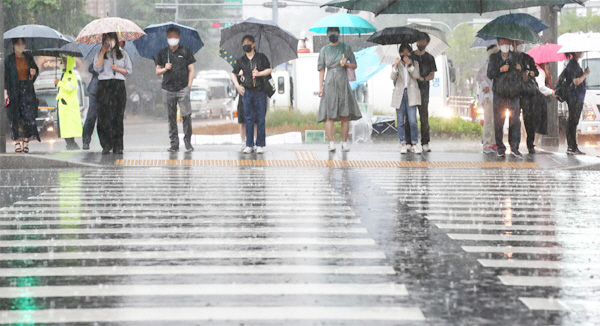 전국적으로 장마가 시작된 23일 서울 광화문에 폭우가 쏟아지는 가운데 시민들이 우산을 쓰고 신호등이 바뀌기를 기다리고 있다. [이충우 기자]