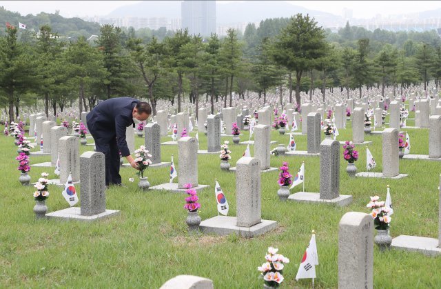 6.25 전쟁 발발 72주년을 하루 앞둔 24일 서울 동작구 국립서울현충원 6.25 전사자 묘역에서 유가족이 장맛비에 넘어진 조화를 다시 꽂고있다.