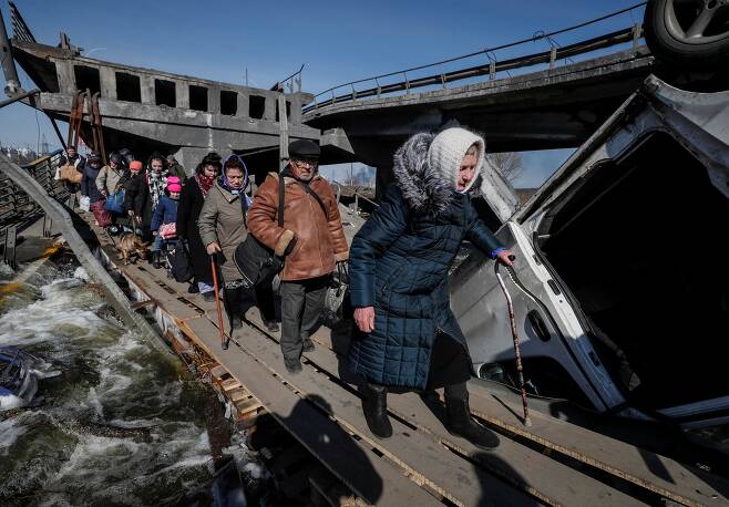 지난 3월 12일 우크라이나 키이우 외곽 이르핀에서 러시아군의 폭격으로 폐허가 된 다리를 피난민들이 아슬아슬하게 건너고 있다./ 로이터 연합뉴스