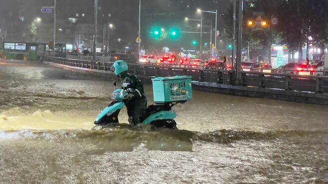 중부지방을 중심으로 폭우가 쏟아진 지난 8일 밤 서울 관악구 도림천이 범람, 주변을 지나는 배달 라이더가 아슬아슬하게 물살을 헤치며 바이크를 옮기고 있다. /뉴스1