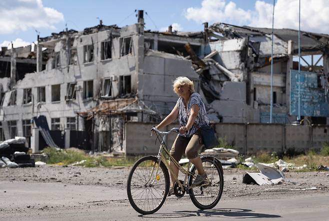 루한스크의 세베로도네츠크에서 7월 24일(현지 시각) 한 여성이 포격으로 파손된 건물을 자전거를 타고 지나가고 있다. /타스통신 연합뉴스