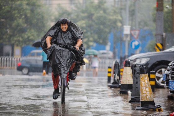 지난달 27일 중국 베이징의 한 거리에서 폭우가 내리는 동안 비닐로 몸을 가린 여성이 자전거를 타고 있다. EPA=연합뉴스