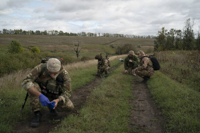 19일(현지시간) 우크라이나 하르키우주 러시아와의 국경 인근 지역에서 우크라이나 방위군이 웅크리고 앉아 우크라이나 병사의 시신이 부비트랩으로 이용됐는지를 확인하고 있다. (사진=뉴시스)