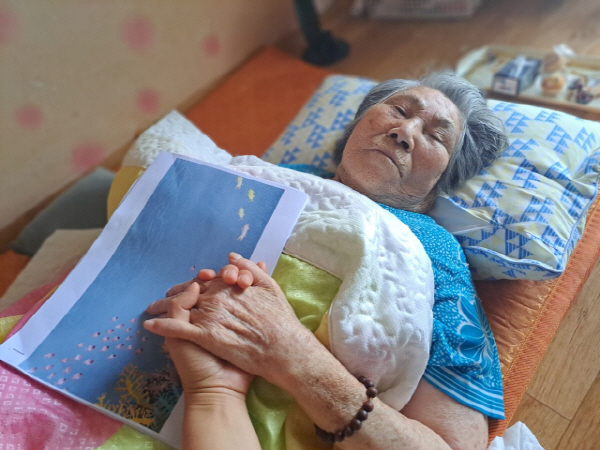 김복례 할머니가 덮은 이불 위 ‘나는 해녀입니다’의 초고가 올려져 있다.