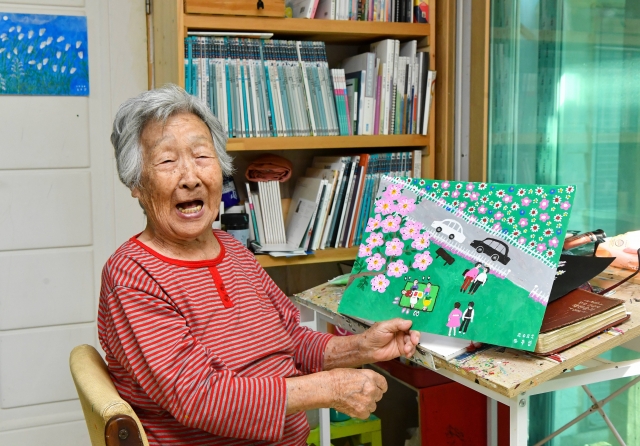 화가 김두엽 할머니가 지난 30일 전남 광양의 자택에서 작품을 들어보이며 웃고 있다. 광양=신석현 포토그래퍼