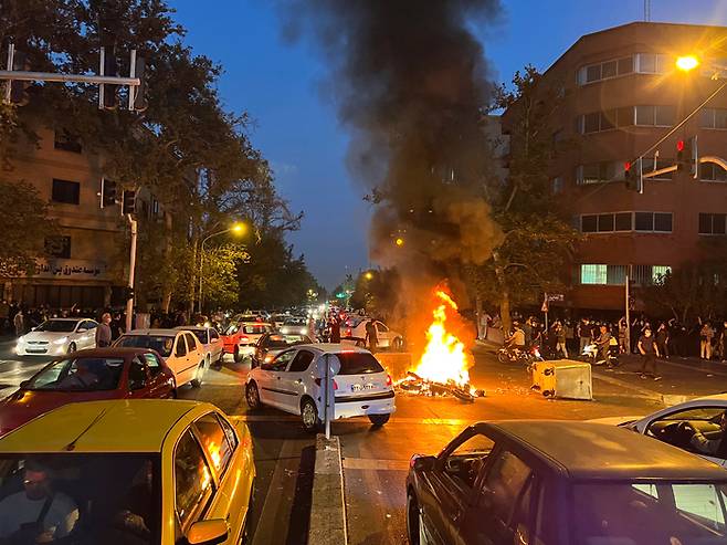 지난달 19일(현지시간) 이란 수도 테헤란 시내에서 ‘히잡 미착용 20대 여성 의문사 사건’에 항의하는 시위가 벌어진 가운데 경찰 오토바이가 불타고 있다. AP연합뉴스