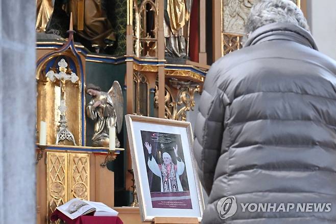 베네딕토 16세의 쾌유 기원하는 신자 (마르크틀 AFP=연합뉴스) 29일(현지시간) 독일 남부 마르크틀의 한 가톨릭 교회에서 한 신자가 베네딕토 16세 전 교황의 사진을 곁에 두고 기도를 올리고 있다. 2022.12.29