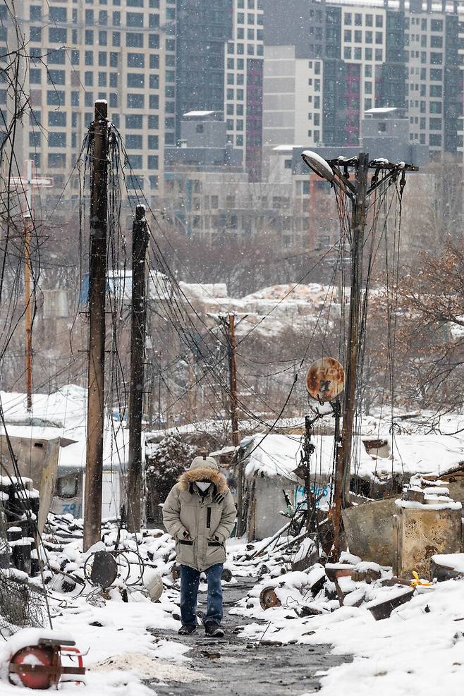 한 이재민이 꼭대기까지 불에 그을린 전봇대 사이로 고개를 숙인 채 걷고 있다.