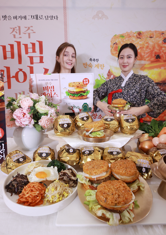 Models pose in front of Lotteria's new Jeonju bibimbap rice burgers at a Lotteria store in Hongdae, western Seoul, on Tuesday morning. The rice burger transforms one of Korea's traditional foods into a burger and is the first of its kind in seven years after Lotteria stopped selling rice burgers in November 2016. [YONHAP]